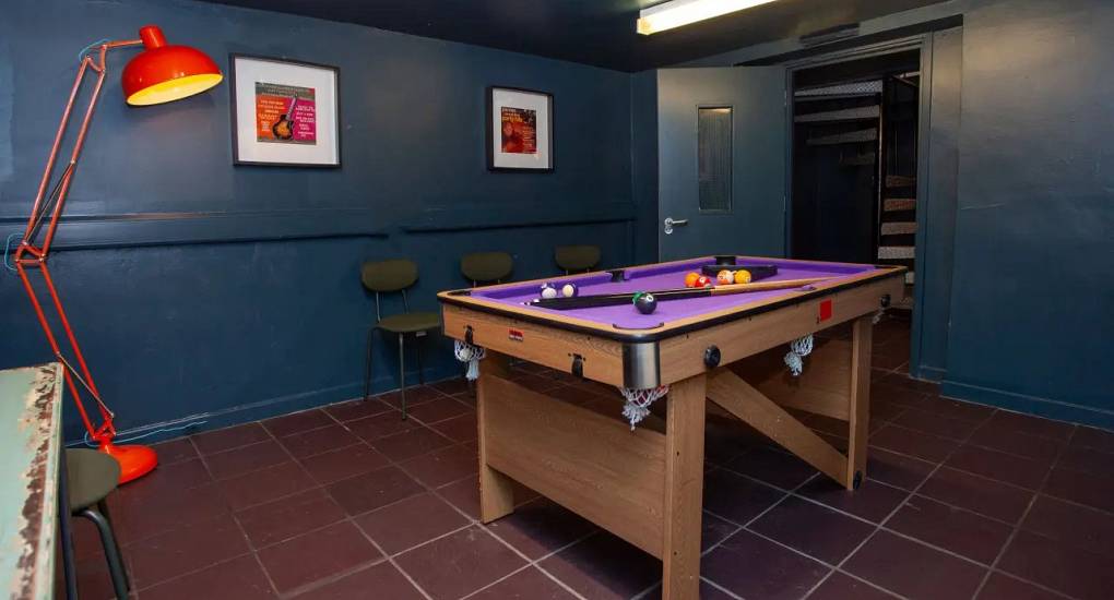 View of the pool table illuminated by a free standing lamp at the Cardiff bunkhouse