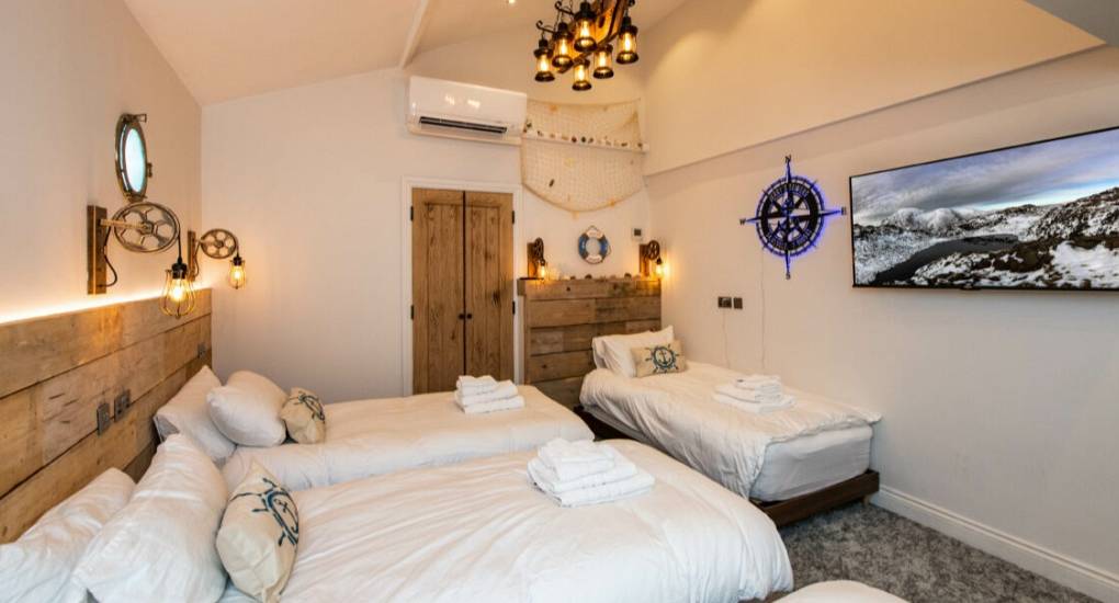 Bedroom showing 3 made up beds with towels at the bottom and tv on the wall