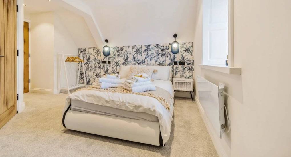Double bed made up in a bedroom with off white decor and pine doors leading to ensuite