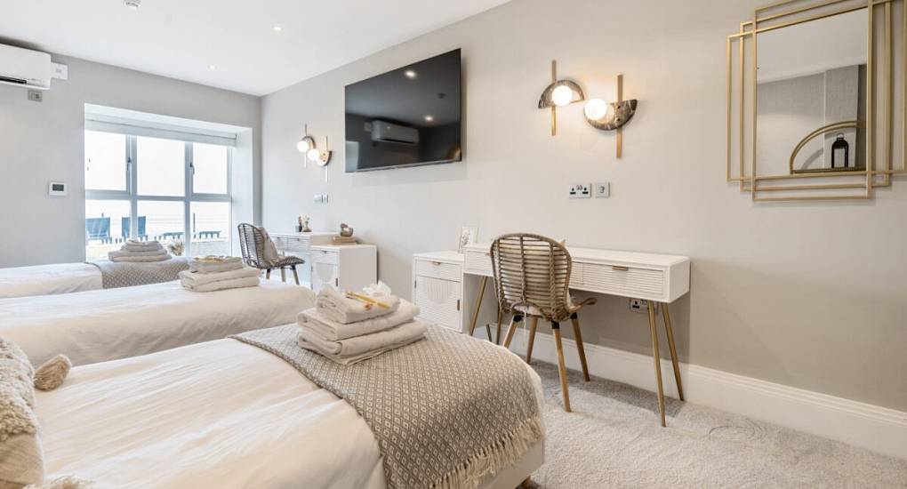 Large bedroom in cream and light brown with two single beds made up ready for guests