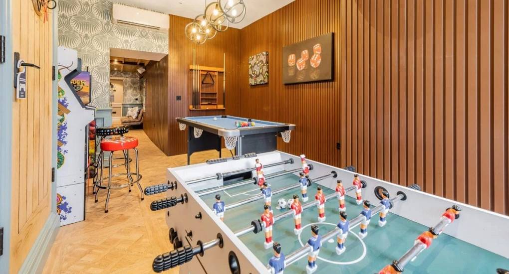 Games room with table football in the foreground and small pool table and arcade machines in the background 