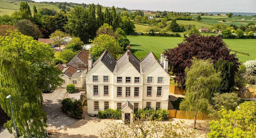 The three-storey cream stone manor exterior and tree-lined gravel driveway at Grand Manor, a large Bath hen party house.