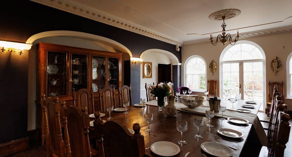 The grand banquet dining room with wooden table at Regal Manor One, a luxury Bath hen party house sleeping 20.