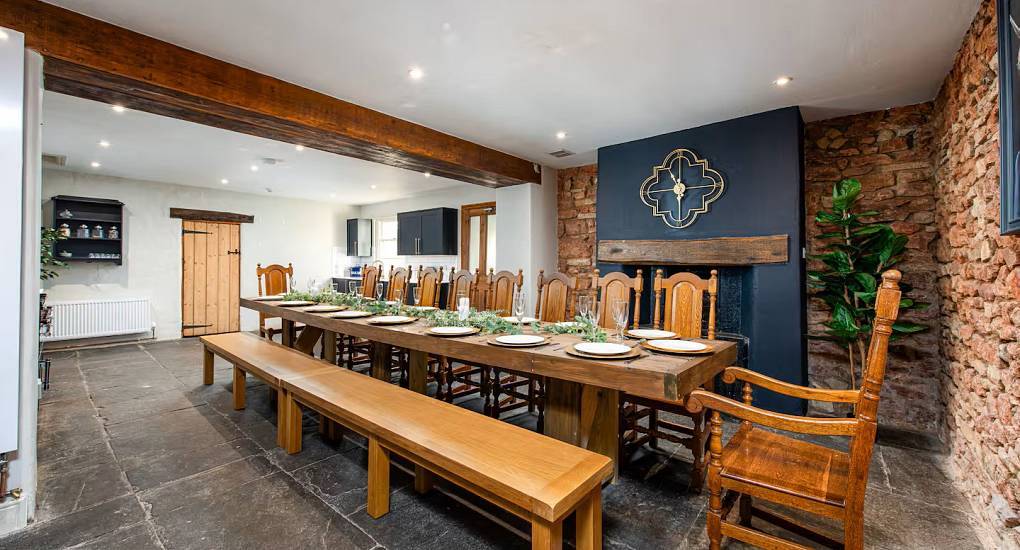 The exposed stone wall dining room with long wooden table at Regal Manor Two, a stylish Bath hen house for 18.
