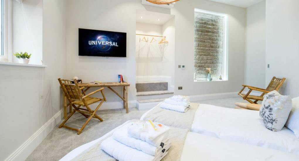 Bedroom in off white with two single beds facing a wall mounted tv