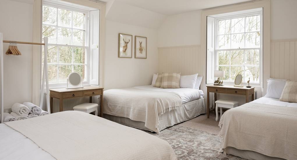 Large bedroom with off white decor with three double beds made up for guests
