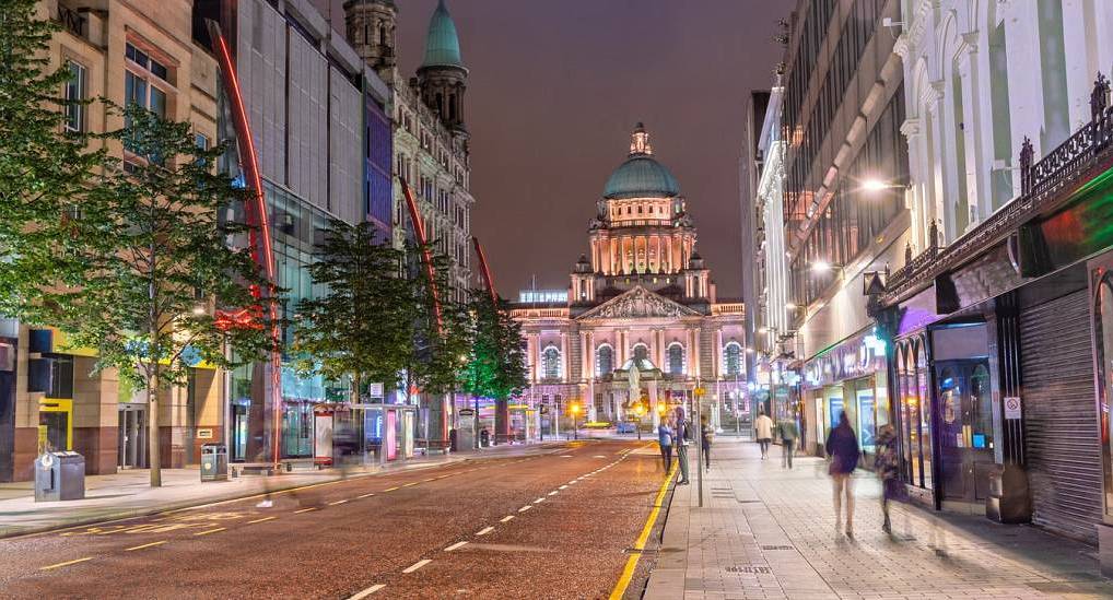 Illuminated Belfast City Hall and streetlights along Donegall Place at night, setting the scene for a belfast hen do.
