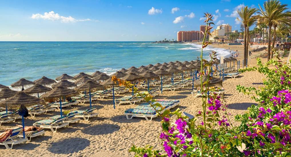 Sandy Benalmadena beach with straw parasols and blue Mediterranean sea, setting the scene for an epic Benalmadena stag do.