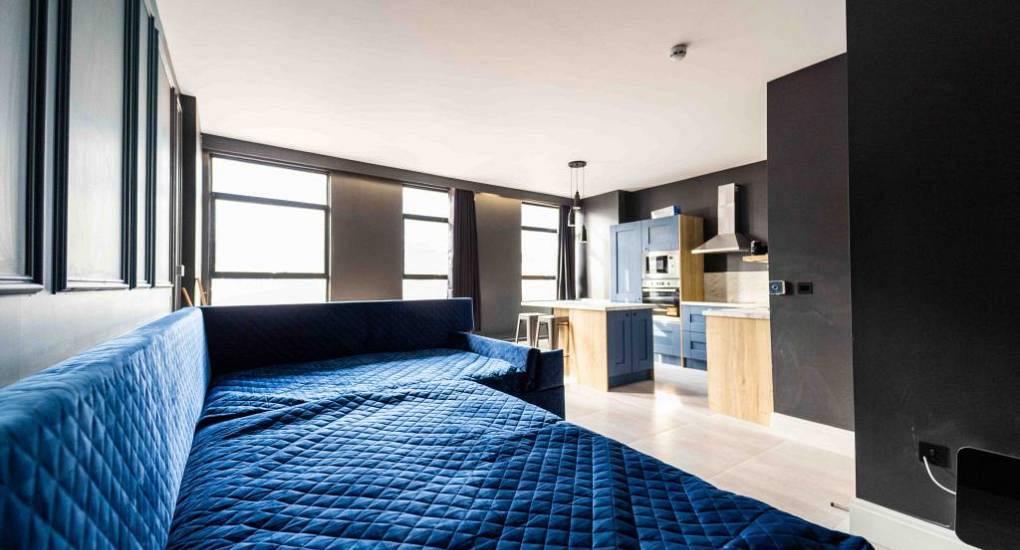 Open-plan living space with royal blue sofa and kitchen at The Luxe, stylish Blackpool centre hen party apartments.
