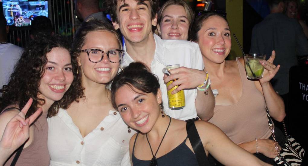 Mixed group of young people on a bar crawl posing with their drinks for the camera