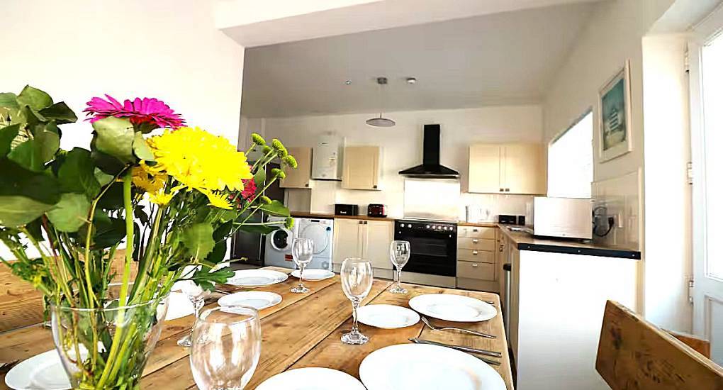 Dining table laid for group meals and kitchen at Charming House, a 5-bedroom Bournemouth hen house sleeping 15.