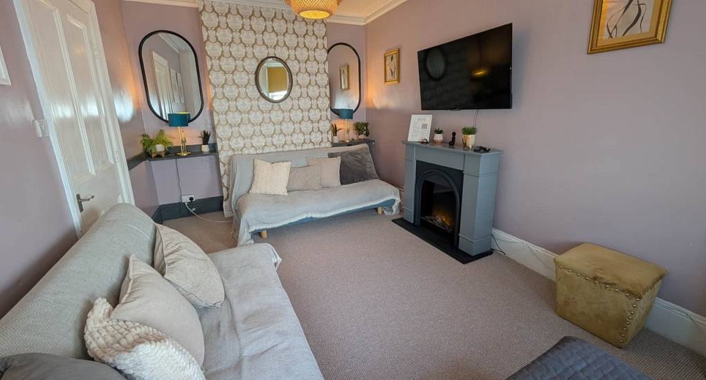 Bohemian lounge with upcycled furniture, open-style fireplace, and large TV at the Bournemouth Hot Tub Garden hen party house.