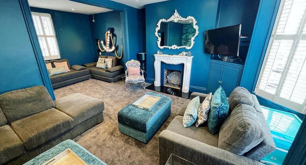 Marine blue living room with plush seating and lit anchor motif at Brighton By The Sea, luxury seafront hen house.