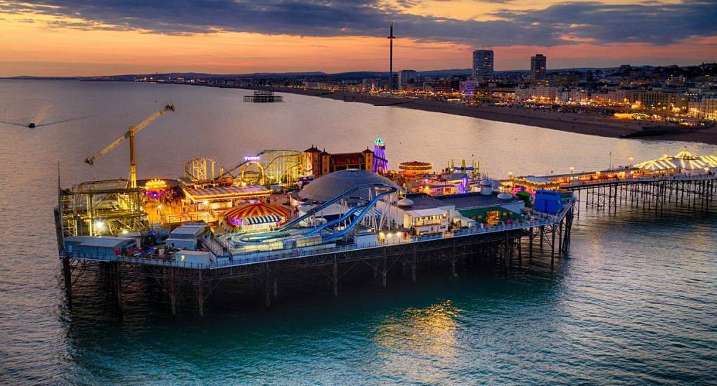 Aerial dusk view of illuminated Brighton Palace Pier rides and ocean sunset, vibrant setting for a Brighton hen do.