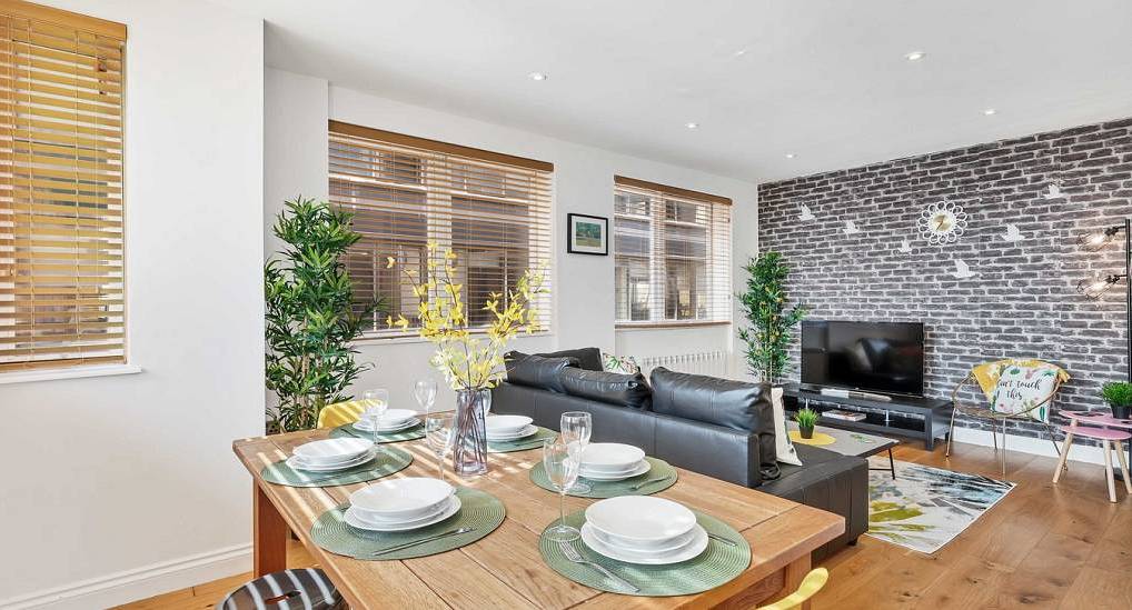 Modern dining table and lounge with grey brick feature wall at Home View, city centre Brighton hen party apartment.