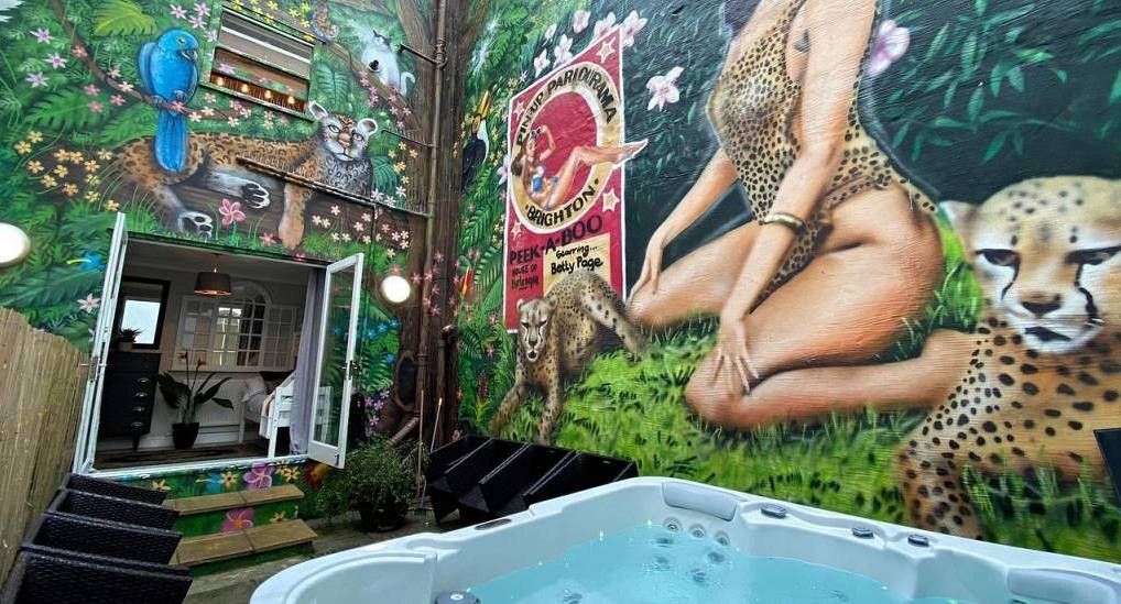 Private outdoor courtyard with 7-seater hot tub and vibrant jungle mural at Hot Tub Gardens, central Brighton hen house.
