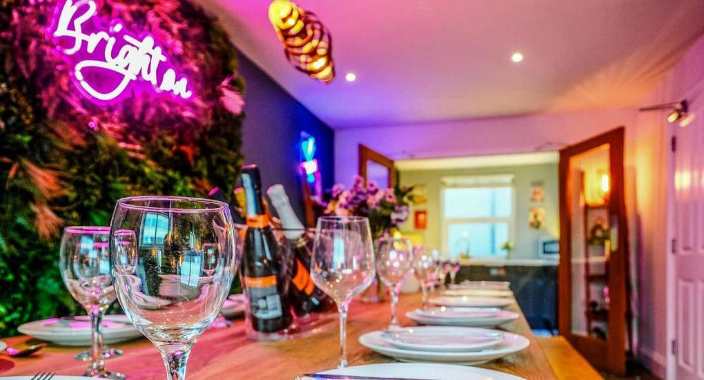 Neon Brighton light setup above group dining table laid with wine glasses at iBrighton, central hen accommodation.