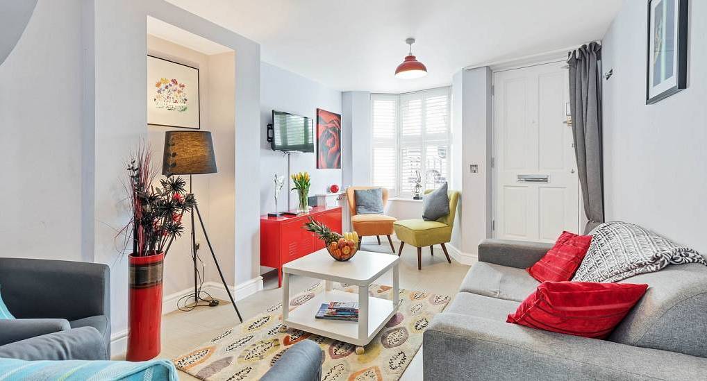 Cozy living room with grey sofa, colorful cushions, and bay window seating at Park House, central Brighton townhouse.