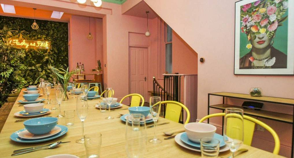 Long dining table laid with blue dishware, pink walls, and neon sign at Pastel House, premier Brighton hen townhouse.