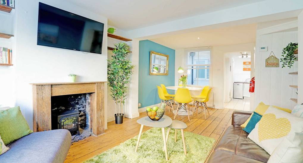 Cosy living room with wood burning stove, yellow dining chairs and teal wall at Sienna Cottage, central Brighton.