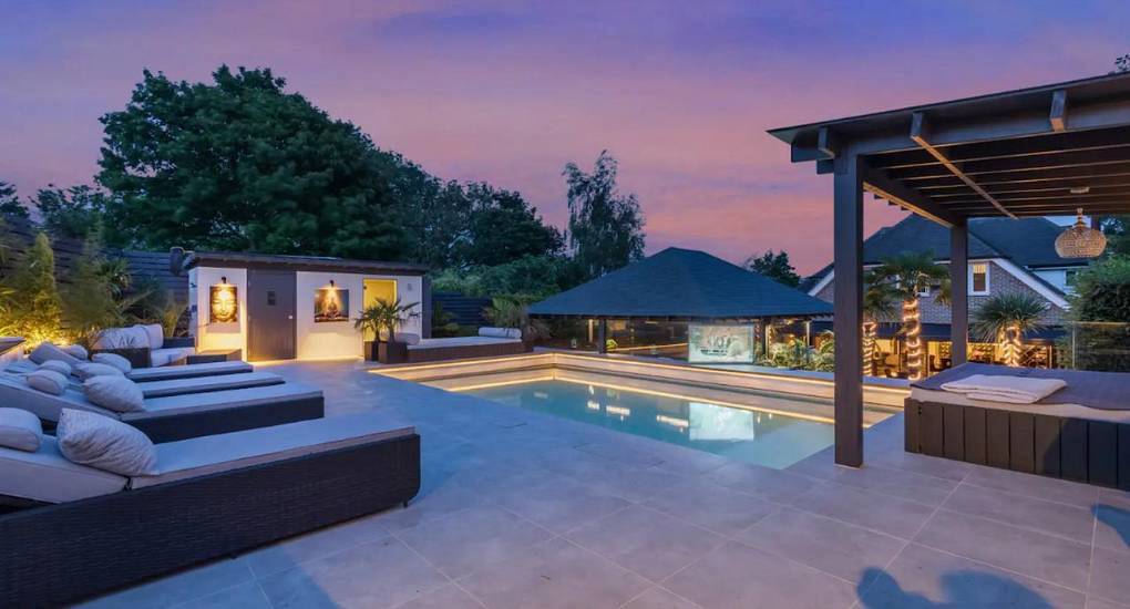 Luxury outdoor swimming pool deck with sun loungers and hot tub at twilight at Sparty House, luxury Brighton villa.