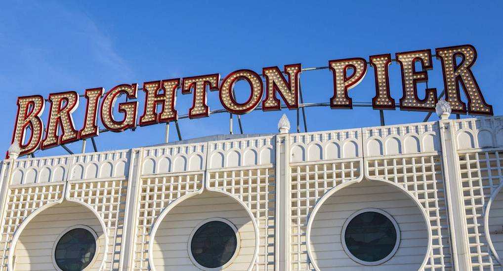 Vintage illuminated Brighton Pier arcade sign under a clear blue sky, setting an iconic scene for a Brighton stag do.