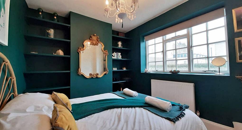 Quirky bedroom with deep emerald green walls, gold ornate mirror and bed at The Ariel, seaside Brighton hen house.