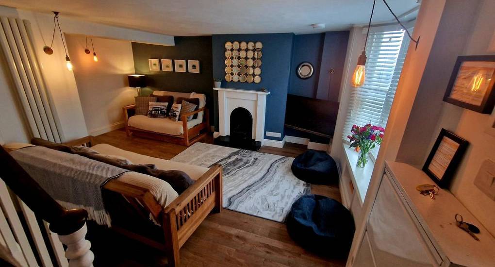Cosy basement lounge with blue feature wall, white fireplace and futons at The Pebbles, hen house near the beach.