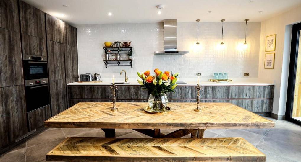 Shabby chic wooden dining table, orange roses and modern dark kitchen at The Shipyard, Brighton hen townhouse.