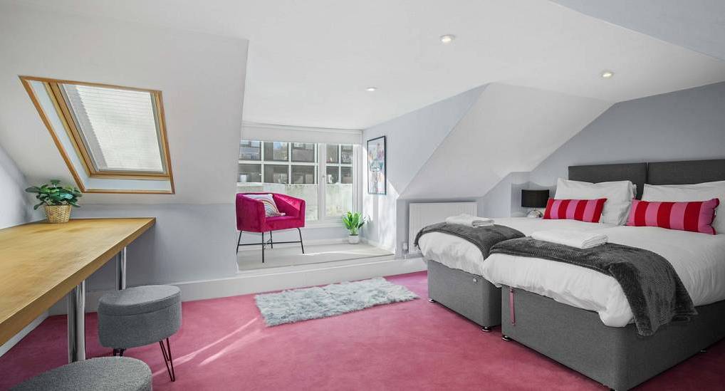 Attic twin bedroom with pink carpet, skylight, and bright lounge chair at The Town House, trendy Brighton hen house.