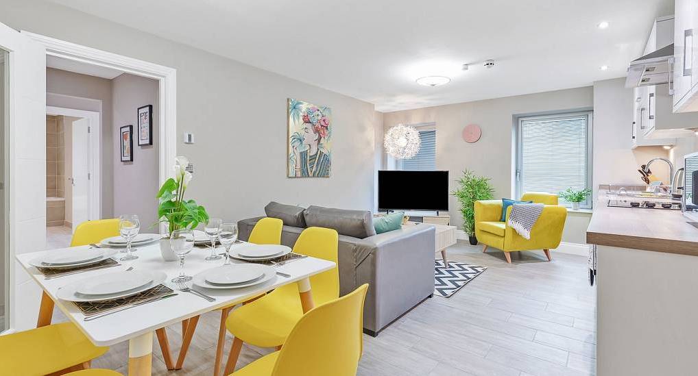 Open plan living area with bright yellow dining chairs and armchair at The Walkers, private central hen apartment.