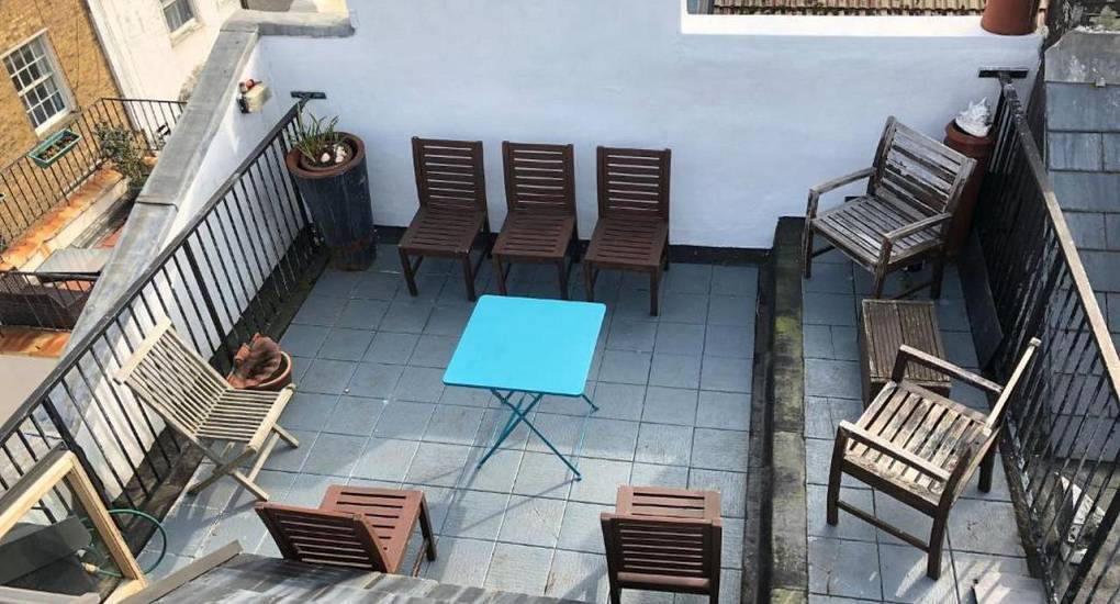 Rooftop deck with wooden patio chairs and bright blue folding table at The Wood, Brighton hen house with terrace.