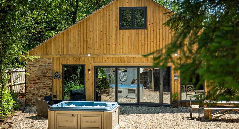 The timber barn exterior and gravel courtyard hot tub at BB Barn, a luxury hen party barn near Bristol and Bath.
