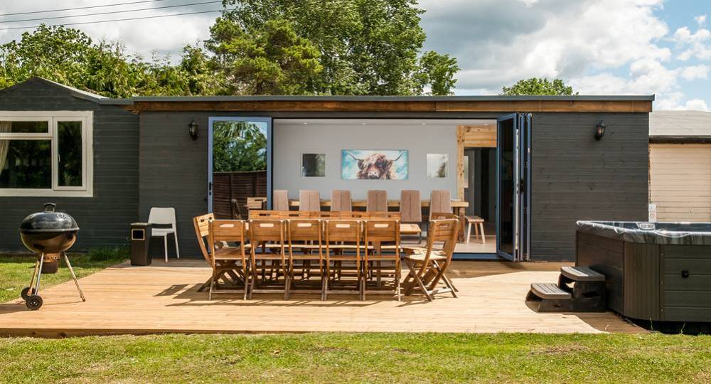 The outdoor patio deck with wooden dining table and grey hot tub at Sanctuary Party House, a Bristol hen house for 18.
