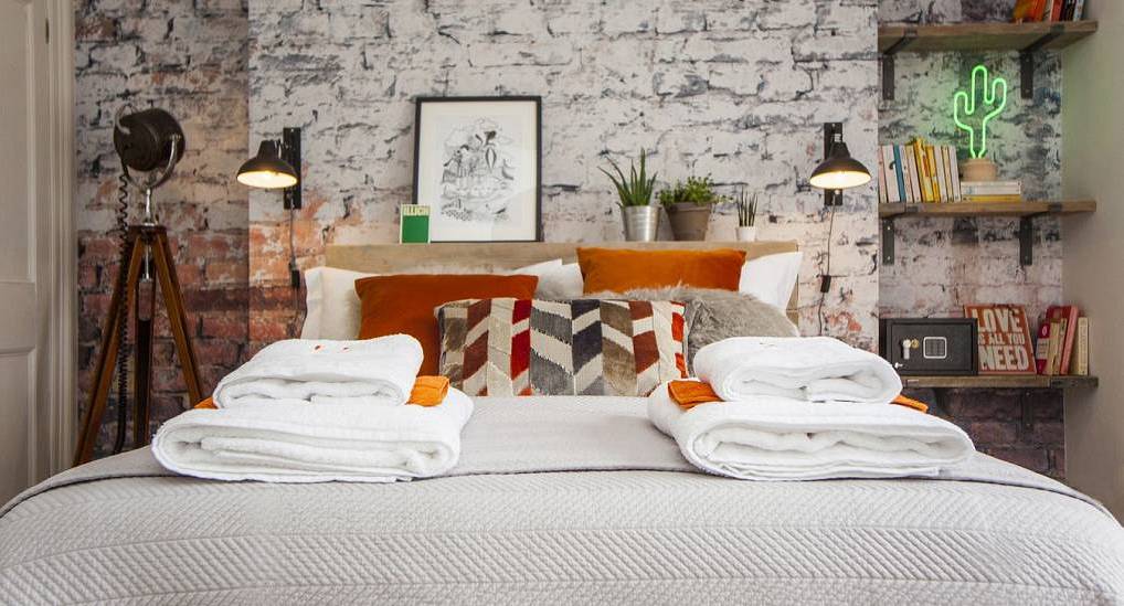The bohemian bedroom with exposed brick wall and neon signs at The Hampton, a central Bristol hen party house.