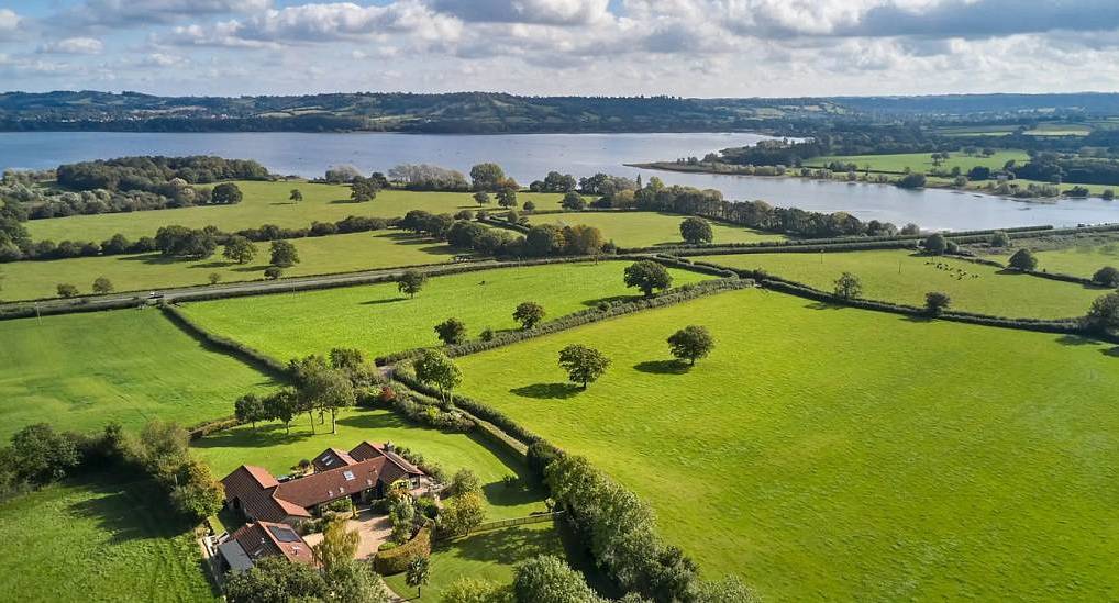 The aerial view of country complex, green fields, and lake at The Retreats, a large Bristol hen party house for 32.