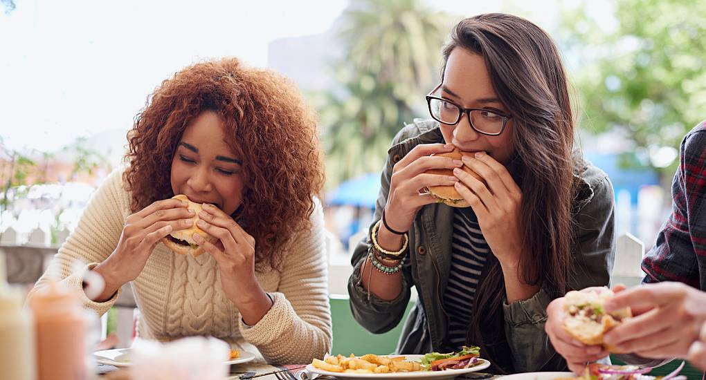 Two young woman eat burger meals