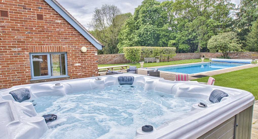 Outdoor hot tub and swimming pool set in expansive lawn garden at Country Haven near Cambridge.