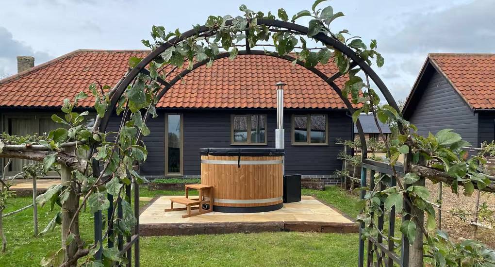 Outdoor wood-fired hot tub framed by garden arch at The Orchard, rural Cambridge hen accommodation.