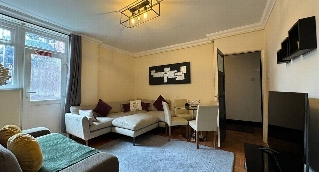 Modern living area with cream corner sofa, glass dining table and TV at Below Deck Fifty, central Cardiff hen apartment.
