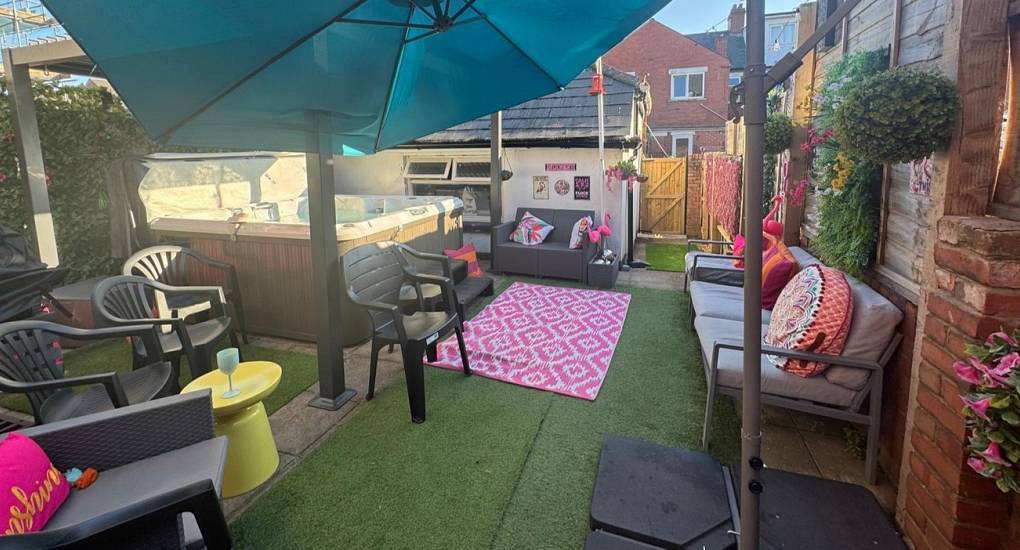 Outdoor courtyard garden with hot tub, parasol shading, and pink patio seating at Flamingo Lounge, Cardiff hen house.