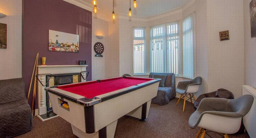 Bright games room with red cloth pool table, fireplace mantel and armchairs at Number Four, central Cardiff hen house.