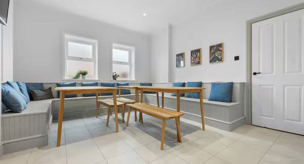 Spacious dining room with L-shaped built-in bench seating and wooden tables at Taff House, central Cardiff hen house.