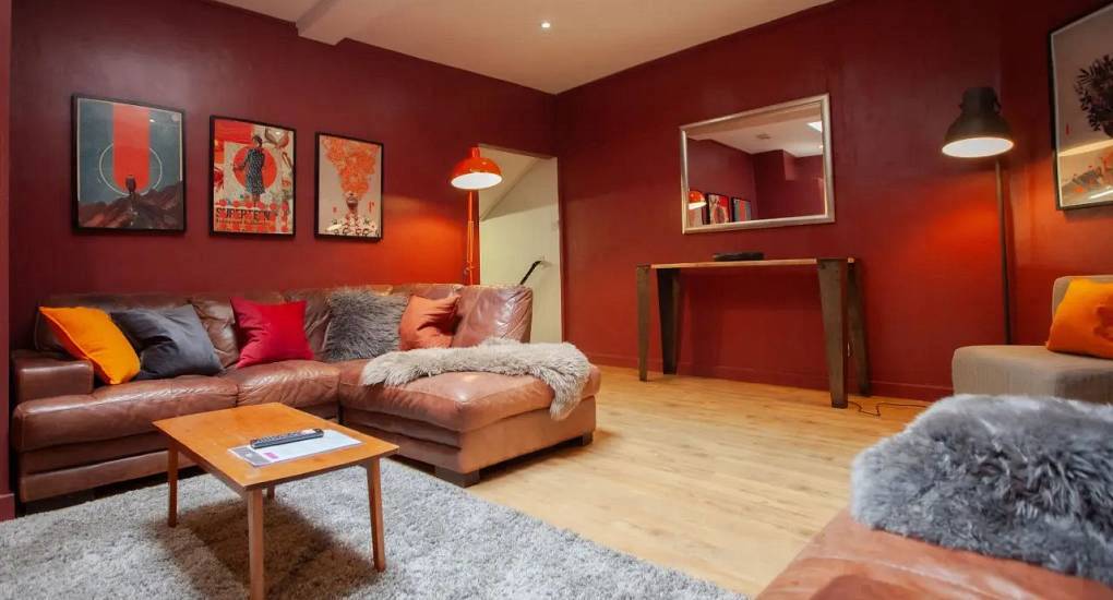 Cosy lounge with deep red walls, brown leather corner sofa and plush cushions at The Bunkhouse, central Cardiff hen house.