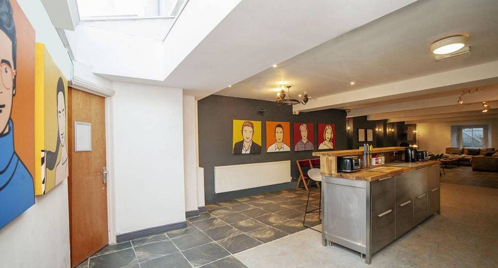 Open plan kitchen with stainless steel island, slate flooring and pop art portraits at The Crown, central Cardiff hen house.