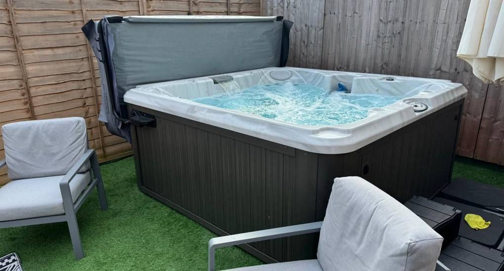 Large outdoor hot tub on artificial lawn patio with grey garden armchairs at The Decks Fifty complex in Cardiff.