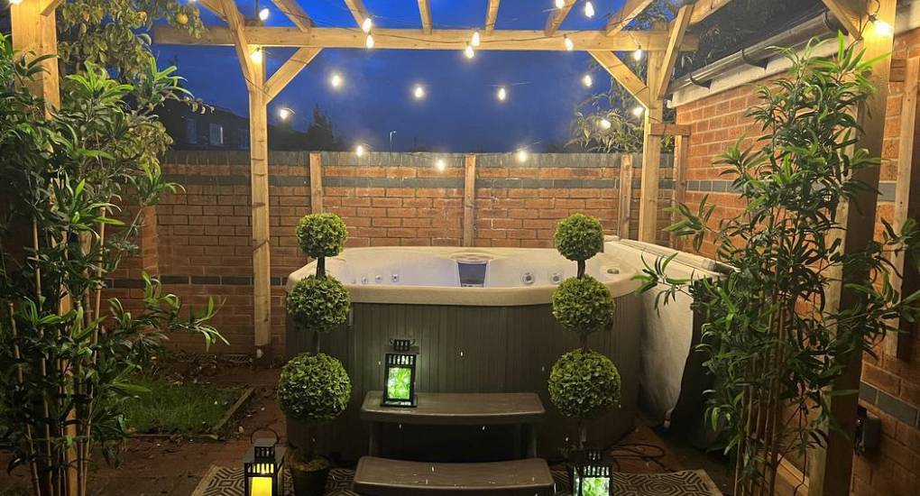 Outdoor hot tub lit by festoon lights under a wooden pergola at Chester Hot Tub 25, spacious Chester hen house.