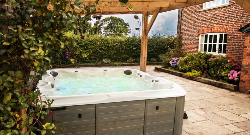 Outdoor hot tub under wooden canopy on stone patio at The Rural Retreat, exclusive hen house near Chester.