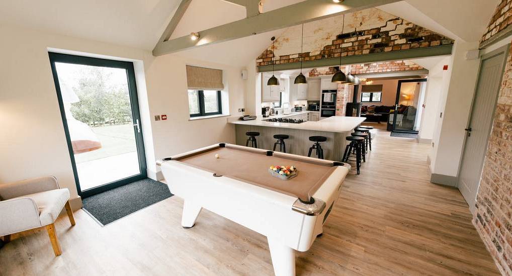 Open plan converted barn with white pool table, breakfast bar and exposed brick walls at Stag and Hen Den Crewe.