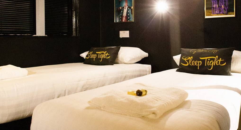 Twin bedroom with dark feature wall and custom Sleep Tight pillows at The Chest, central Chester hen party house.